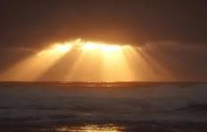 Sun rays breaking through clouds over the ocean.